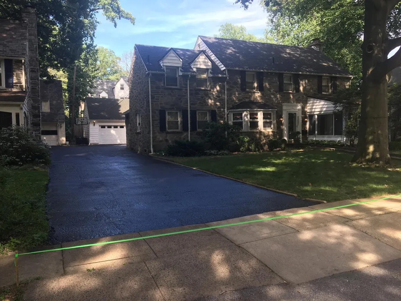 A stone colonial in Delaware County, Pennsylvania, with its asphalt driveway freshly sealcoated to a deep black finish and a clean edge against the lawn.