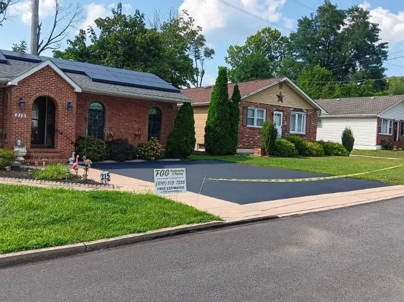 A brick home with a newly sealcoated driveway, taped off with yellow caution tape and an FGG yard sign.