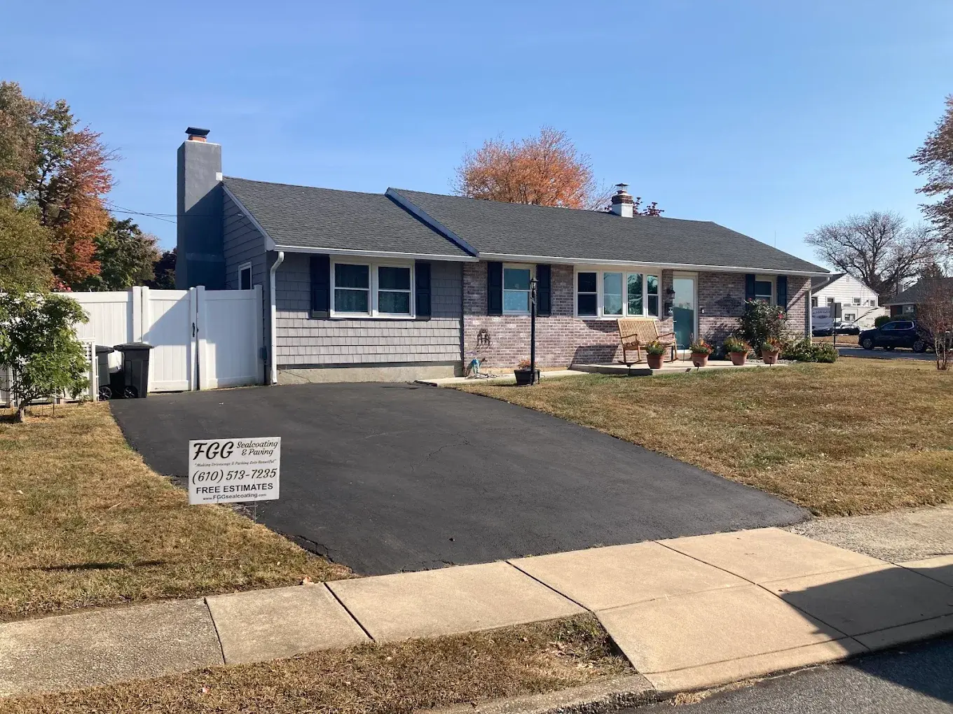 A ranch home with a freshly sealcoated driveway and an FGG Sealcoating & Paving yard sign at the curb.